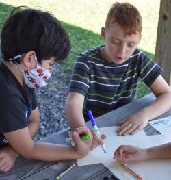 Two children sitting at a picnic table and coloring.