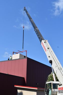 A crane lifting a large square HVAC unit onto a roof. 